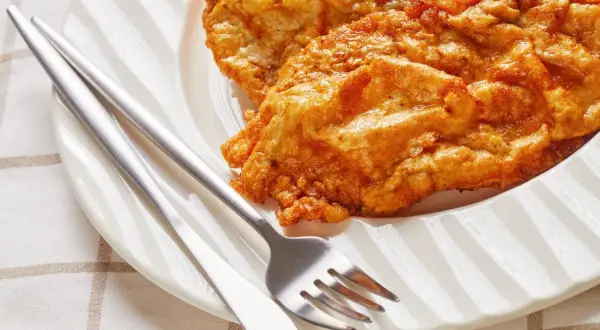 Złocisty kotlet słoneczny, chrupiący i apetyczny, czeka na talerzu z widelcem i nożem.