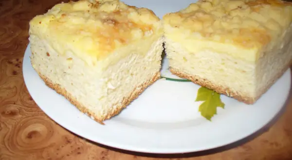Puszyste ciasto drożdżowe z serem, z kruszonką na wierzchu, pokrojone na dwa kawałki na białym talerzu.
