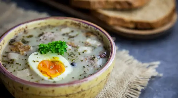 Pyszny żurek z kiełbasą i ziemniakami, ozdobiony jajkiem i natką. Zastanawiasz się, ile kcal ma żurek z kiełbasą i ziemniakami?