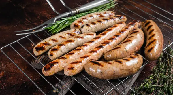 Aromatyczna biała kiełbasa z grilla, rumiana i soczysta, z ziołami i widelcem do serwowania.