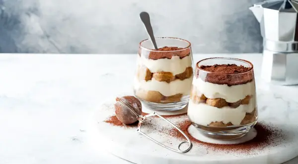 Dwa pucharki z kremowym, warstwowym deserem, posypane kakao. To najprostsze tiramisu, idealne na deser.