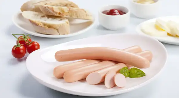 Parówki drobiowe na talerzu z pieczywem i pomidorkami. Czy cukrzyk może jeść parówki drobiowe? Odpowiedź zależy od składu i ilości.