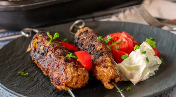 Dwa soczyste kofta kebab na patyczkach, podane z pomidorami i kremowym sosem.