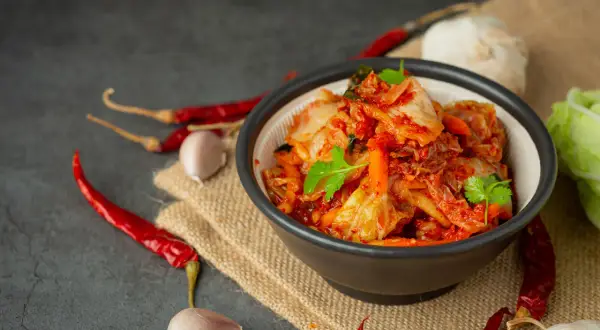 Miseczka pełna pikantnego, czerwonego kimchi, z suszonymi papryczkami chili i czosnkiem w tle. To tradycyjne koreańskie danie, które warto poznać!