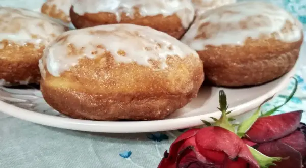 Pączki z ziemniakami Ewy Wachowicz, oblane lukrem, kuszą na talerzu. Obok leży czerwona róża.
