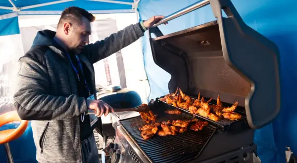 Mężczyzna przygotowuje pyszne skrzydełka i mięso na grillu. Idealne grillowanie w słoneczny dzień.