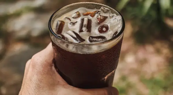 Dłoń trzyma szklankę orzeźwiającego napoju z lodem. To idealny sposób na ochłodę, gdy zastanawiasz się, cold brew co to.