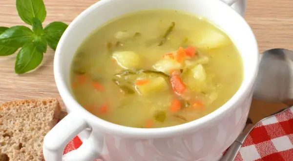 Zupa ogórkowa Ani gotuje się w białej misce, obok kromki chleba i gałązki bazylii.