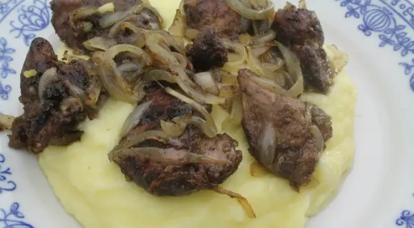 Pyszna wątróbka drobiowa z cebulką na kremowym purée ziemniaczanym, podana na talerzu z niebieskim wzorem.
