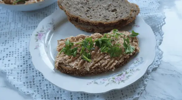 Na talerzu z różanym wzorem leży kromka ciemnego chleba z pastą jajeczną i natką pietruszki. Obok druga kromka, a w tle miseczka z pastą. Taka pyszna awanturka na śniadanie!