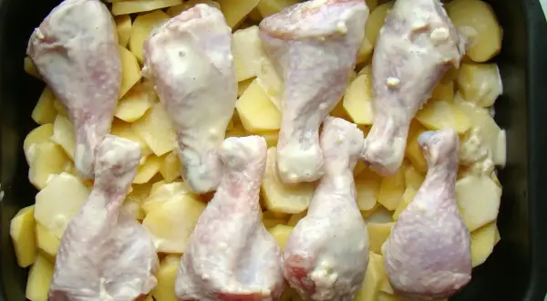 Pałki kurczaka w sosie, ułożone na ziemniakach w naczyniu żaroodpornym. Idealne do pieczenia, by uzyskać chrupiące danie.