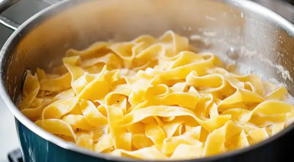 Szeroki, żółty makaron tagliatelle gotuje się w bulgoczącej wodzie. Idealny sposób, jak ugotować makaron do ulubionego sosu.