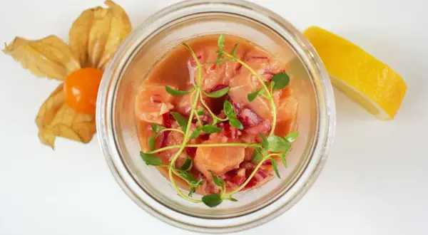 Pyszne ceviche z łososia w szklanym naczyniu, ozdobione świeżymi ziołami, z cytryną i physalis w tle.