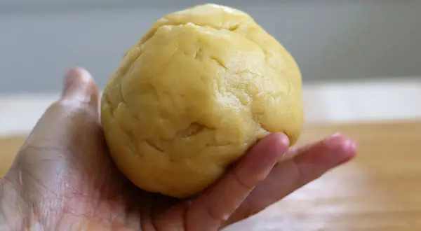 Kruche ciasto do szarlotki w dłoni, gotowe do rozwałkowania. Idealna baza dla pysznego deseru.
