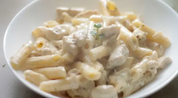 Penne z kurczakiem w kremowym sosie śmietanowym, udekorowane gałązką ziół. Pyszne danie gotowe do podania.