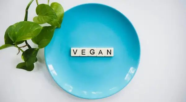 Niebieski talerz z literami "VEGAN" i zielonymi liśćmi. To symbol tego, co to jest weganizm: dieta bez produktów odzwierzęcych.