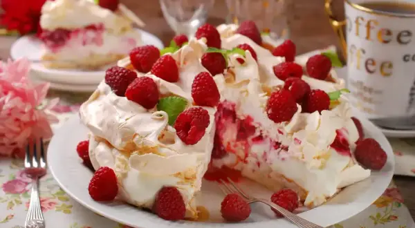 Pyszny tort bezowy z mascarpone i bitą śmietaną, ozdobiony malinami. Idealny na deser!
