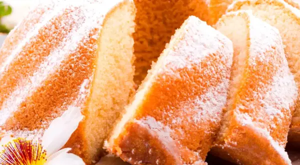 Szybka babka wilgotna, oprószona cukrem pudrem, z widocznymi kawałkami ciasta i ozdobiona kwiatem.