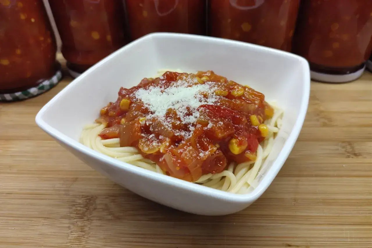 Porcja spaghetti z sosem buffalo, posypana parmezanem. W tle słoiki z domowym sosem.