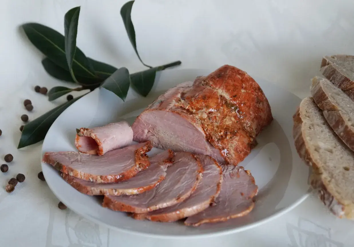 Soczysta kiełbasa z łopatki z szynkowara, pokrojona w plastry, podana z chlebem i liśćmi laurowymi.