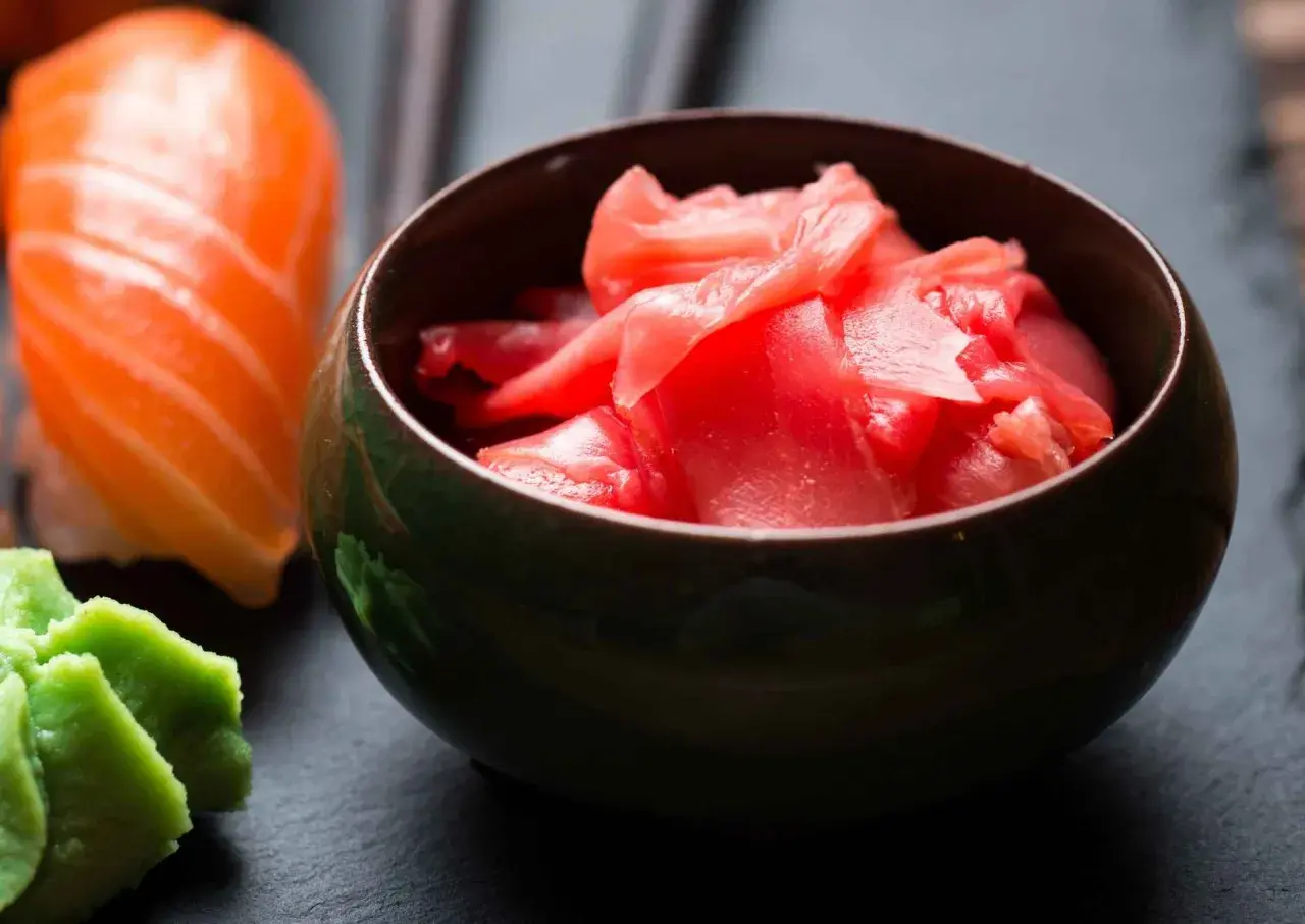 Miseczka z różowym, marynowanym imbirem obok sushi i wasabi. Idealny dodatek do japońskich potraw.