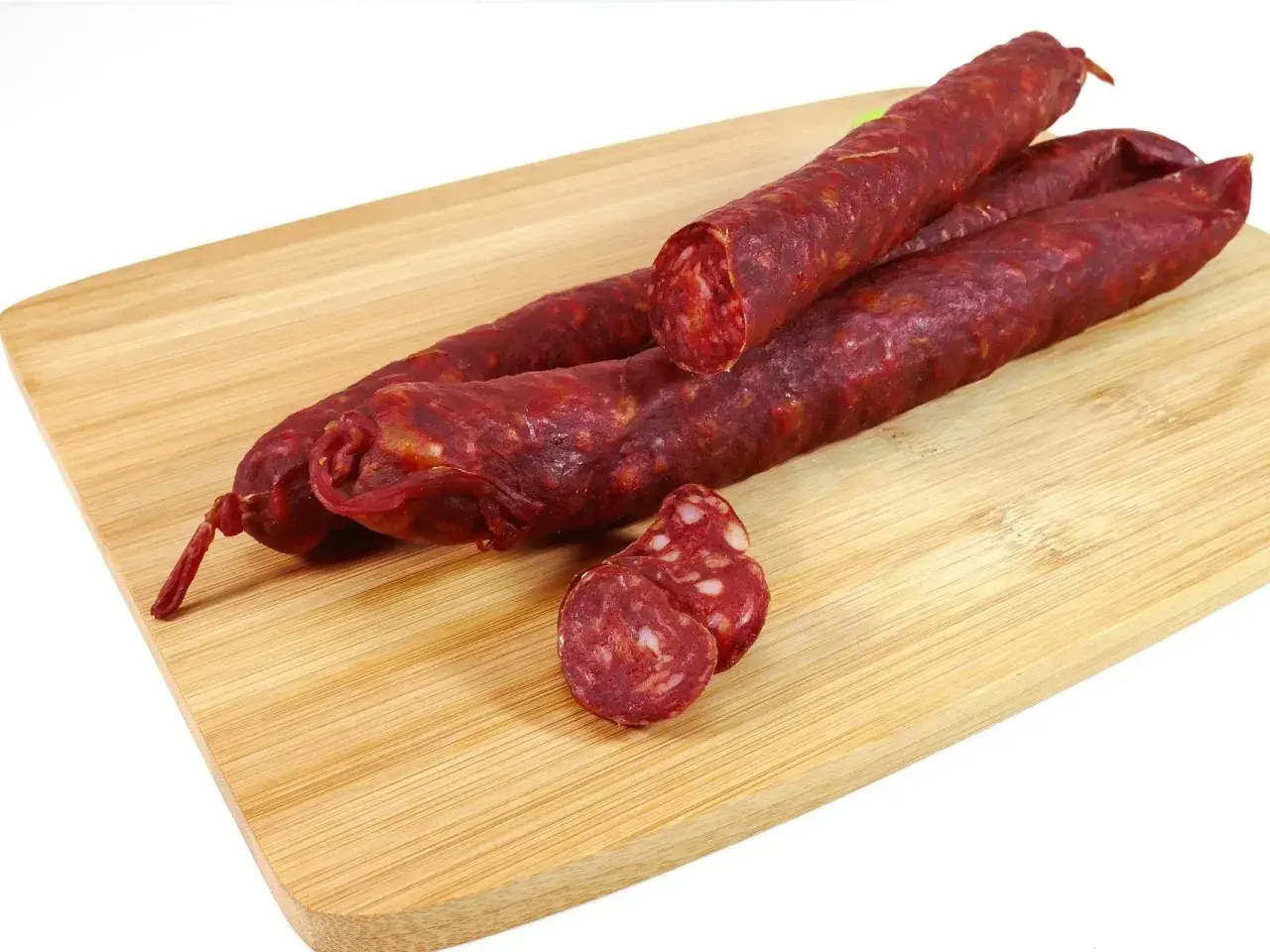 Trzy długie kiełbaski chorizo leżą na drewnianej desce. Jedna jest przekrojona, ukazując charakterystyczne kawałki mięsa i tłuszczu.