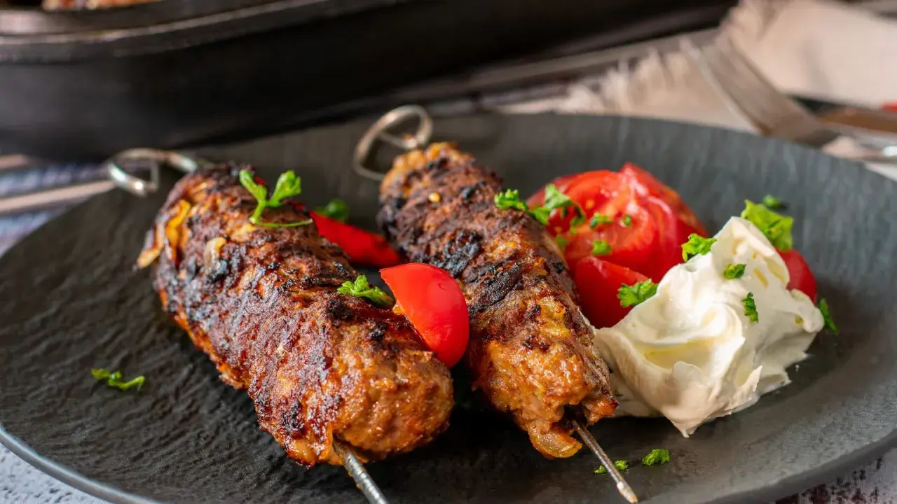 Dwa soczyste kofta kebab na patyczkach, podane z pomidorami i kremowym sosem.