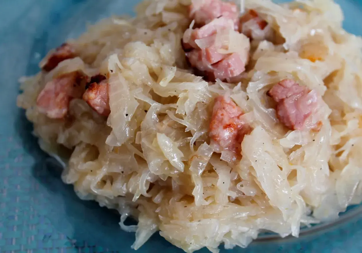 Kapusta kiszona zasmażana z boczkiem, podana na talerzu. Aromatyczne danie, które rozpływa się w ustach.