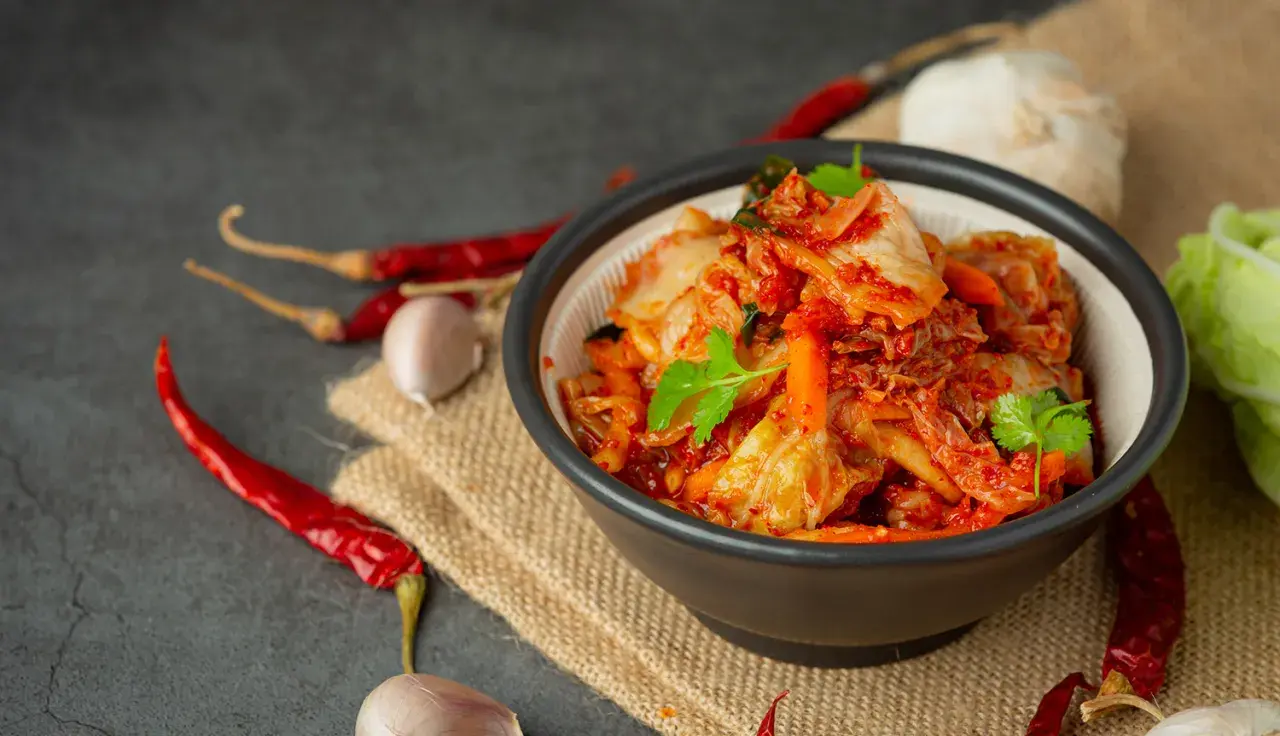 Miseczka pełna pikantnego, czerwonego kimchi, z suszonymi papryczkami chili i czosnkiem w tle. To tradycyjne koreańskie danie, które warto poznać!