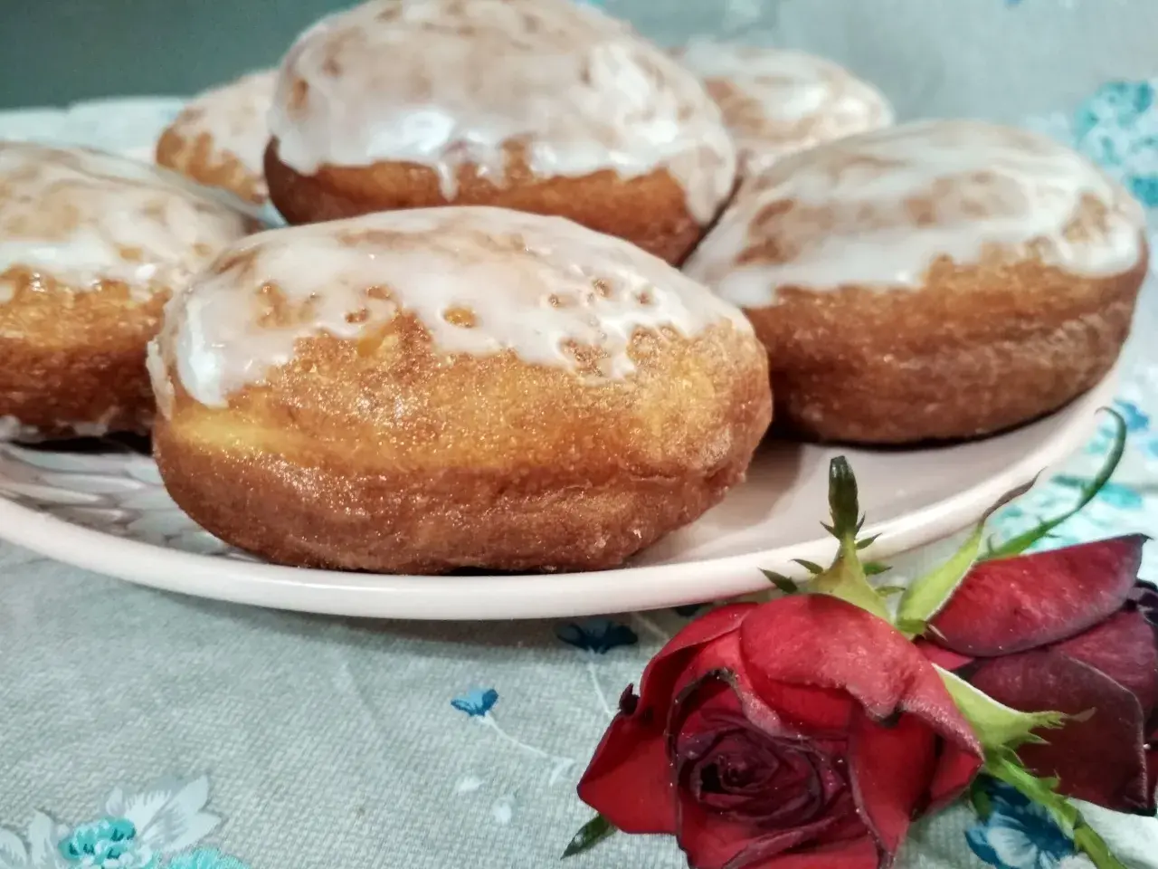 Pączki z ziemniakami Ewy Wachowicz, oblane lukrem, kuszą na talerzu. Obok leży czerwona róża.