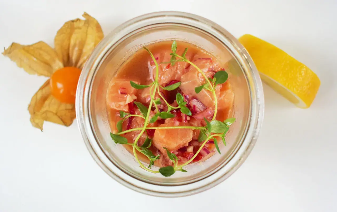 Pyszne ceviche z łososia w szklanym naczyniu, ozdobione świeżymi ziołami, z cytryną i physalis w tle.