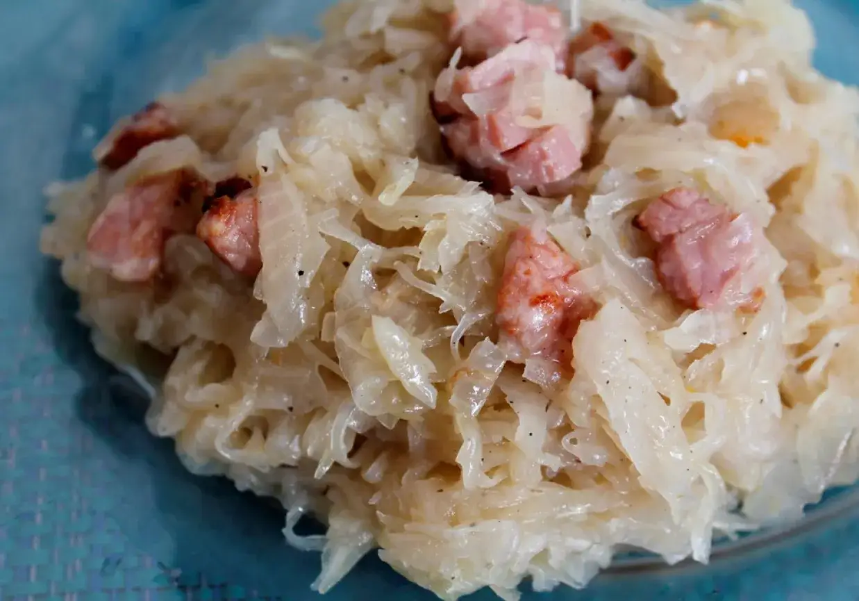 Kapusta kiszona zasmażana z boczkiem, podana na talerzu. Aromatyczne danie, które rozpływa się w ustach.