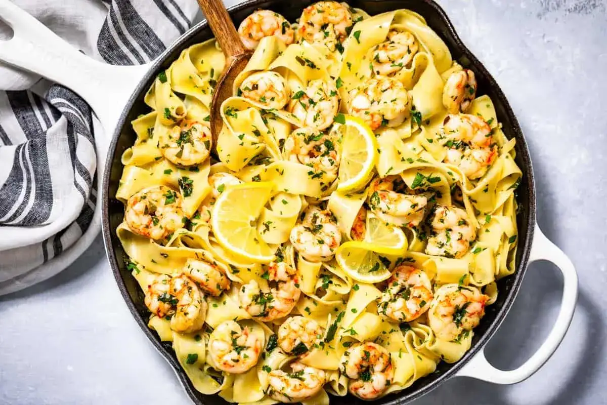 Pappardelle z krewetkami, czosnkiem i pietruszką, skropione cytryną, podane w patelni.