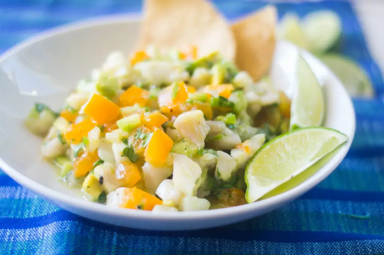 Pyszne ceviche z kawałkami ryby, pomarańczy i awokado, podane z limonką i chipsami kukurydzianymi.