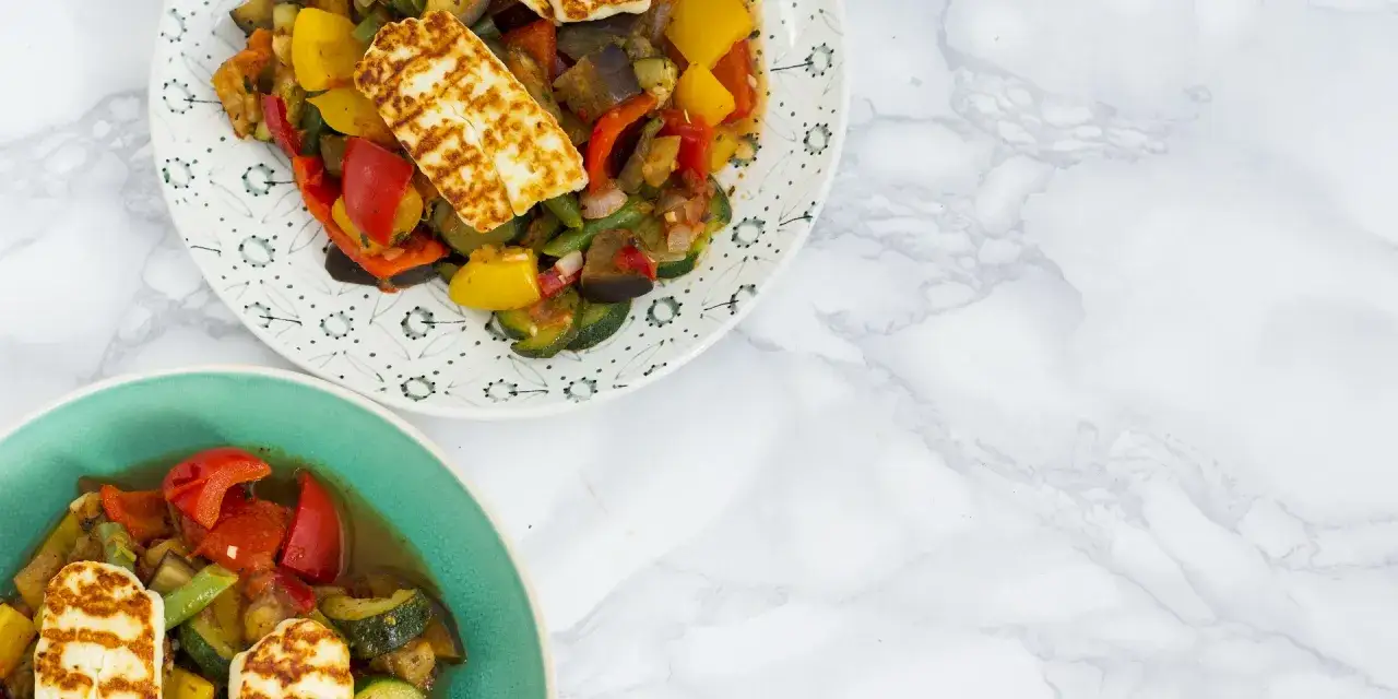 Dwa talerze z warzywami z grilla i grillowanym serem halloumi.