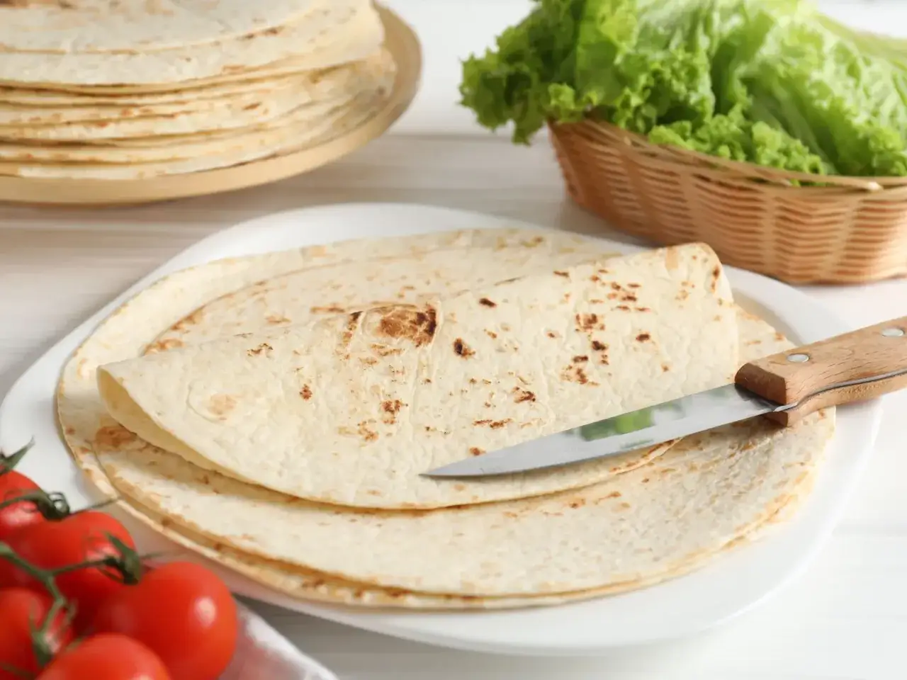 Placki tortilla oryginalny przepis na talerzu, obok pomidorki i sałata.