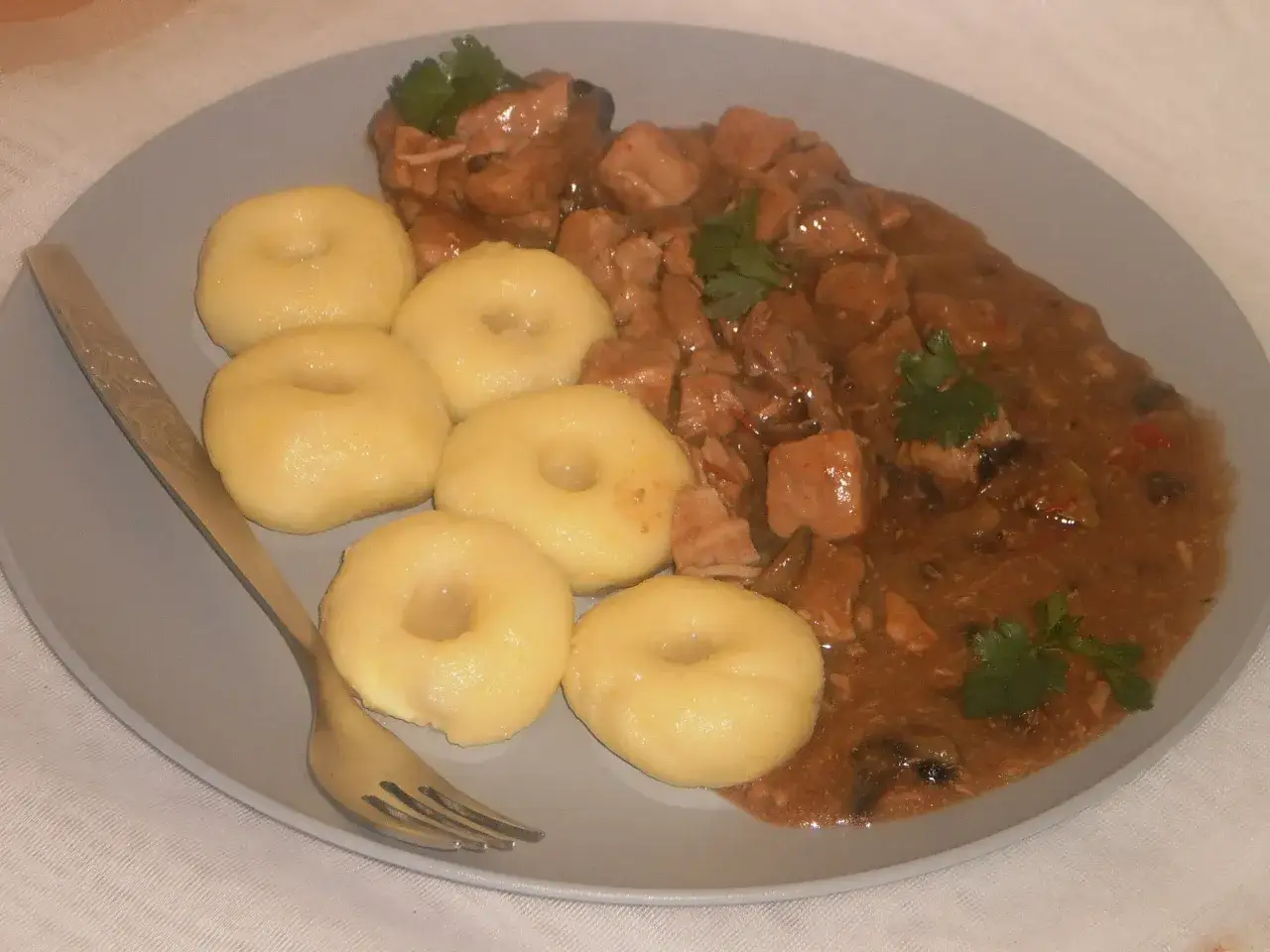 Pyszne kluski śląskie z gęstym, aromatycznym sosem mięsnym, ozdobione natką pietruszki. Idealny obiad.