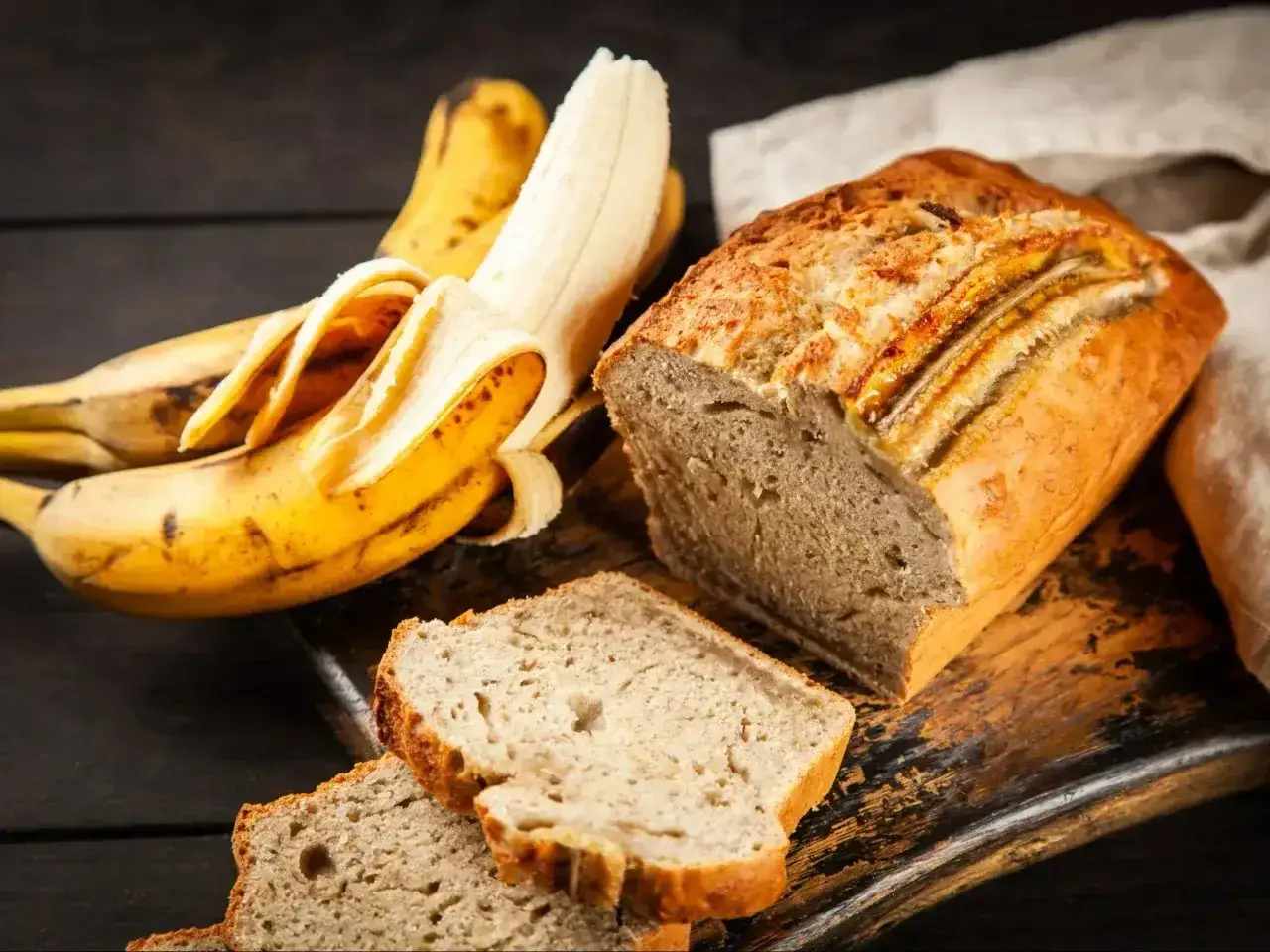 Wilgotne ciasto bananowe, z kawałkami bananów na wierzchu, obok dojrzałych bananów.