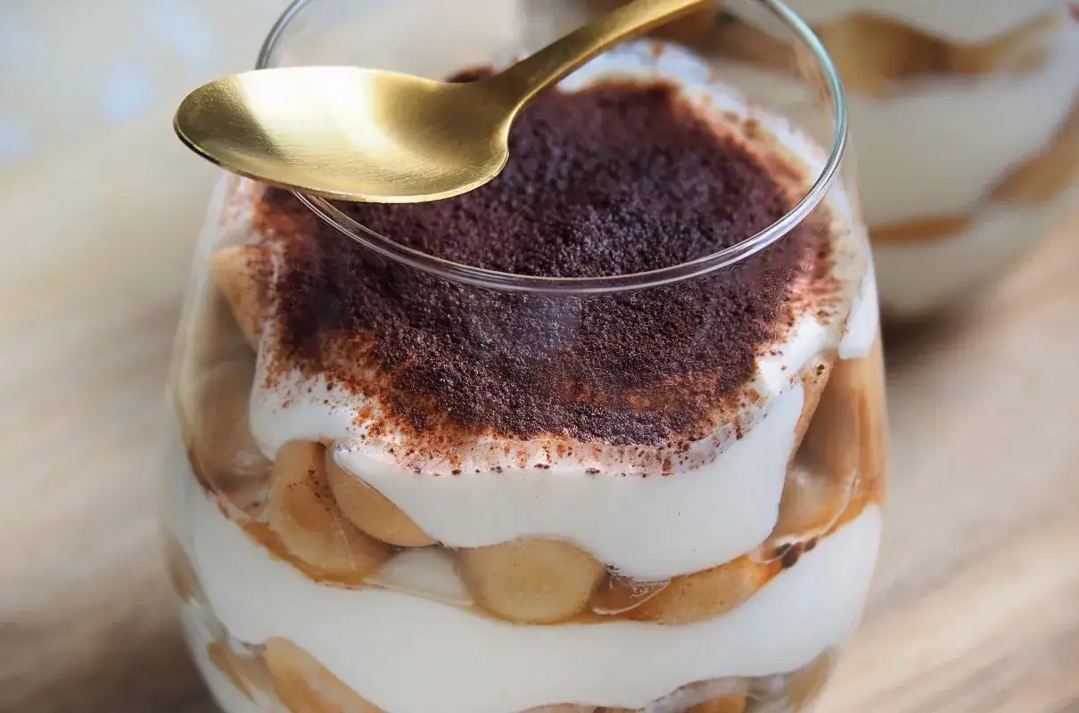 Pyszne tiramisu z mascarpone w szklance, posypane kakao. Złota łyżeczka czeka na pierwszy kęs tego sprawdzonego przepisu.