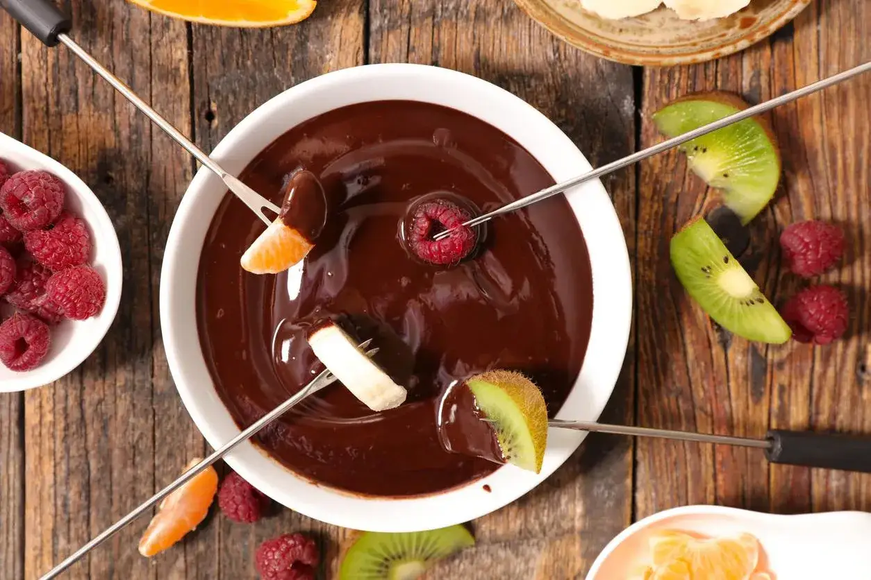 Pyszne owoce w czekoladzie: maliny, kiwi, banan i mandarynka zanurzane w gorącym sosie czekoladowym.