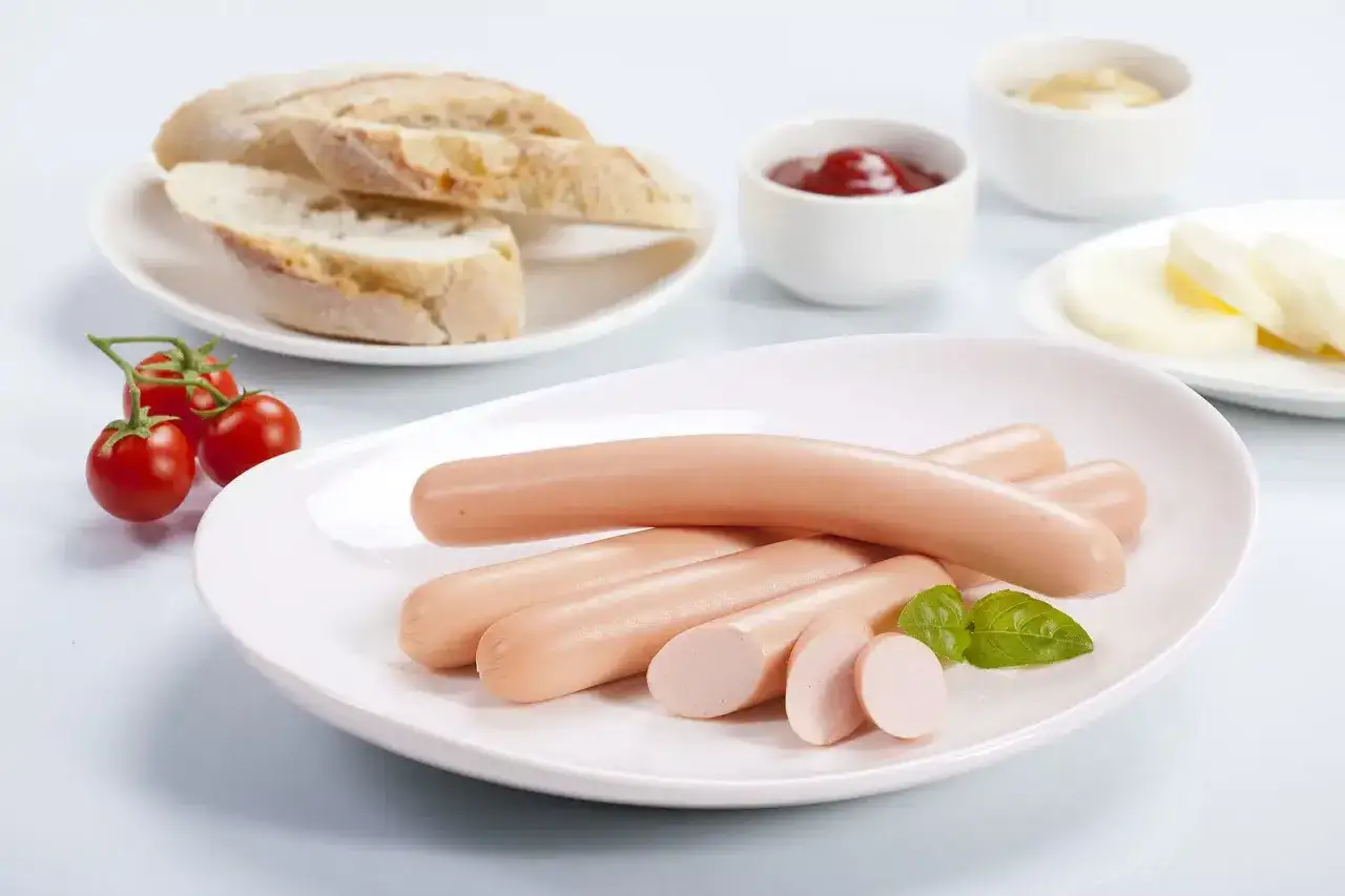Parówki drobiowe na talerzu z pieczywem i pomidorkami. Czy cukrzyk może jeść parówki drobiowe? To pytanie nurtuje wiele osób dbających o dietę.