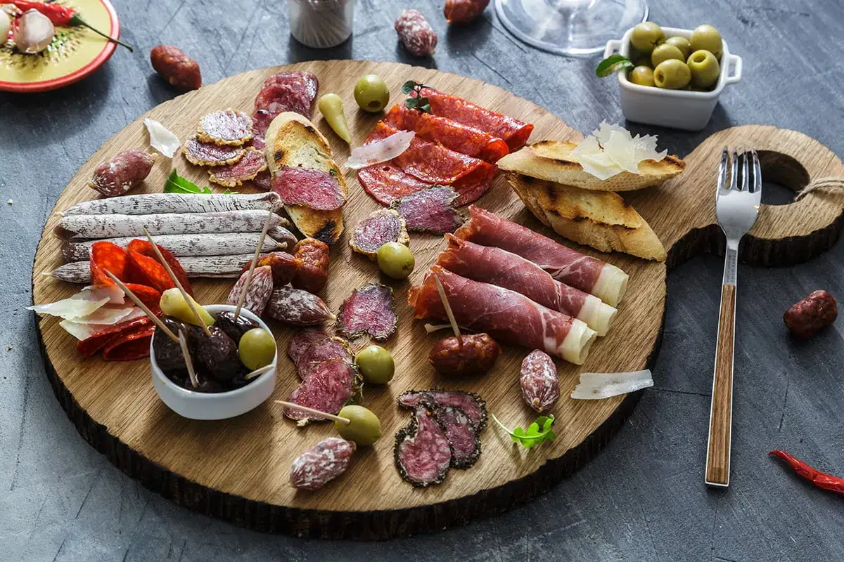 Deska wędlin: salami, szynka, oliwki, pieczywo. Zastanawiasz się, chorizo co to? To pikantna hiszpańska kiełbasa, idealna na przekąskę.