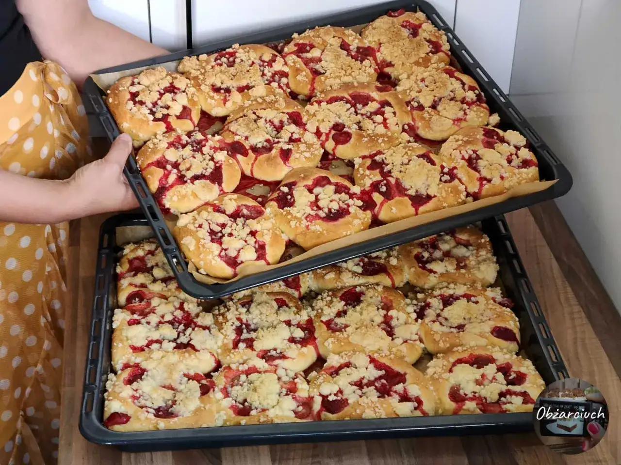 Dwie blachy pełne pysznych, domowych drożdżówek z truskawkami i kruszonką, gotowe do pieczenia lub podania.