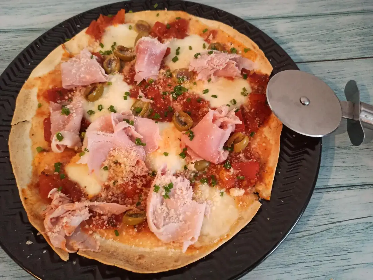 Pyszna pizza z tortilli na patelni, z szynką, oliwkami i parmezanem, gotowa do pokrojenia.