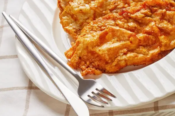 Złocisty kotlet słoneczny, chrupiący i apetyczny, czeka na talerzu z widelcem i nożem.
