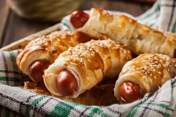 Chrupiące parówki w cieście francuskim z serem żółtym, posypane sezamem, podane w koszyku.