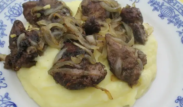Pyszna wątróbka drobiowa z cebulką na kremowym purée ziemniaczanym, podana na talerzu z niebieskim wzorem.