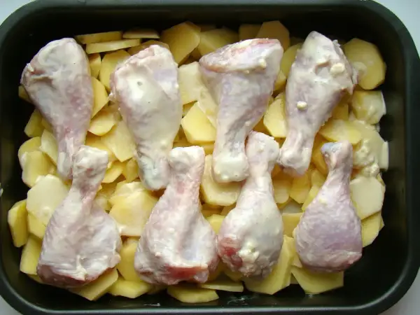 Pałki kurczaka w sosie, ułożone na ziemniakach w naczyniu żaroodpornym. Idealne do pieczenia, by uzyskać chrupiące danie.
