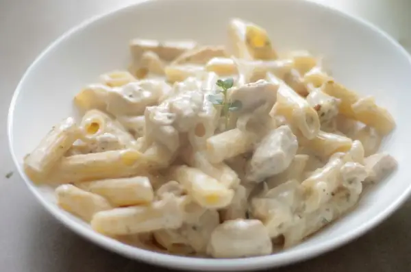 Penne z kurczakiem w kremowym sosie śmietanowym, udekorowane gałązką ziół. Pyszne danie gotowe do podania.
