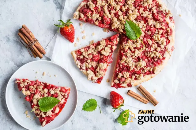 Pyszna tarta z truskawkami i kruszonką, ozdobiona miętą, obok laski cynamonu i świeżych truskawek. Idealna na letnie popołudnie.